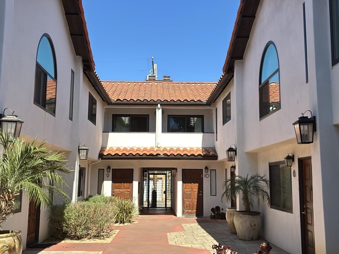 Wide exterior view of a multi-story stucco residential complex with a concrete and paver courtyard at ground level showing slab-on-grade construction