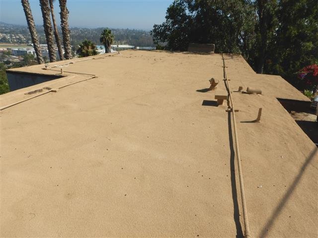 Broad flat gravel roof surface with palm trees and city valley view in the background