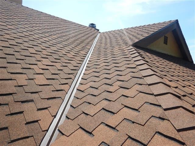 Inspector's-eye view looking up the sloped shingle roof ridge with a dormer visible against blue sky