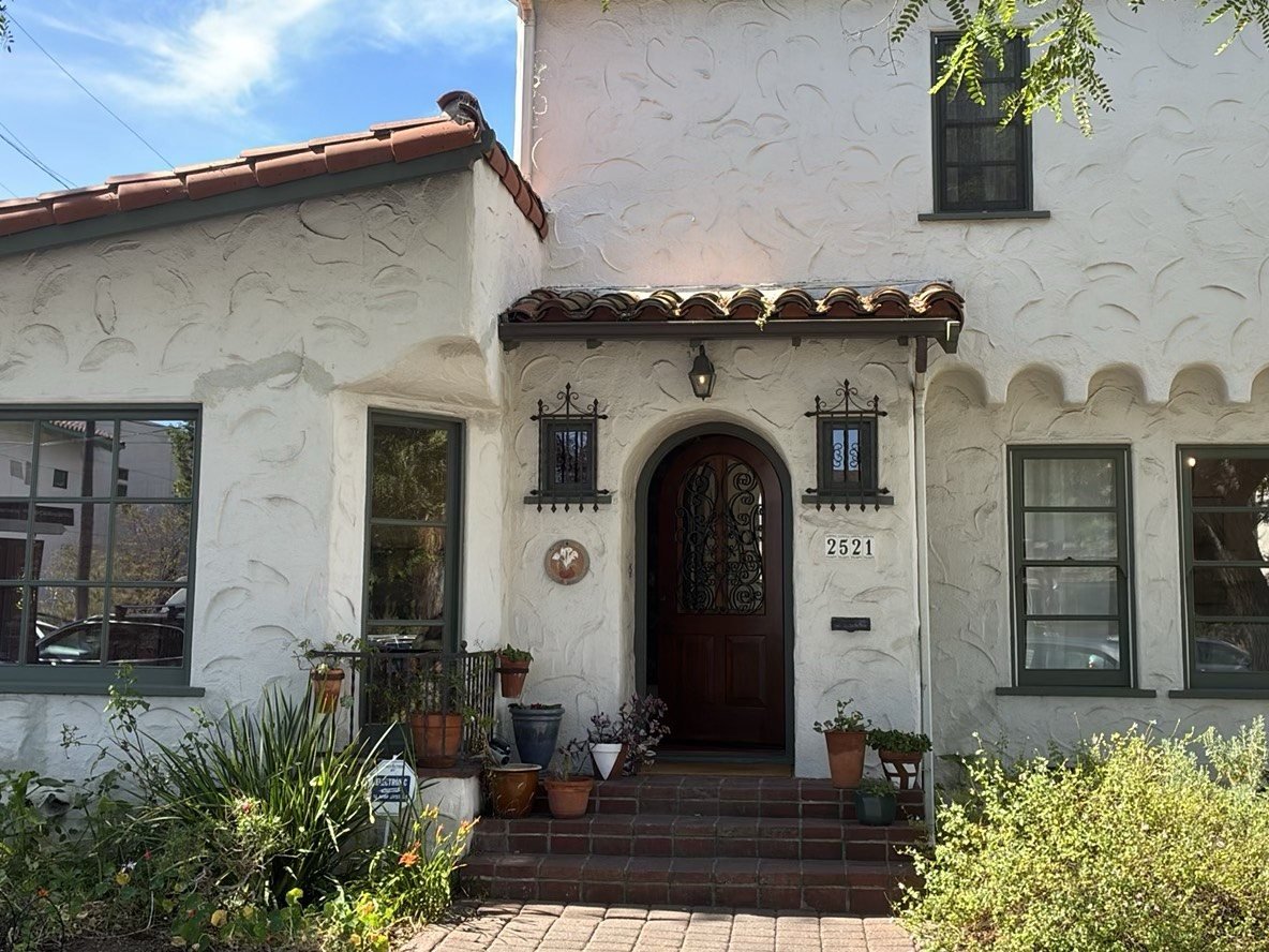 Front exterior of a charming Spanish Colonial stucco home with terracotta roof and lush landscaping, address 2521 visible