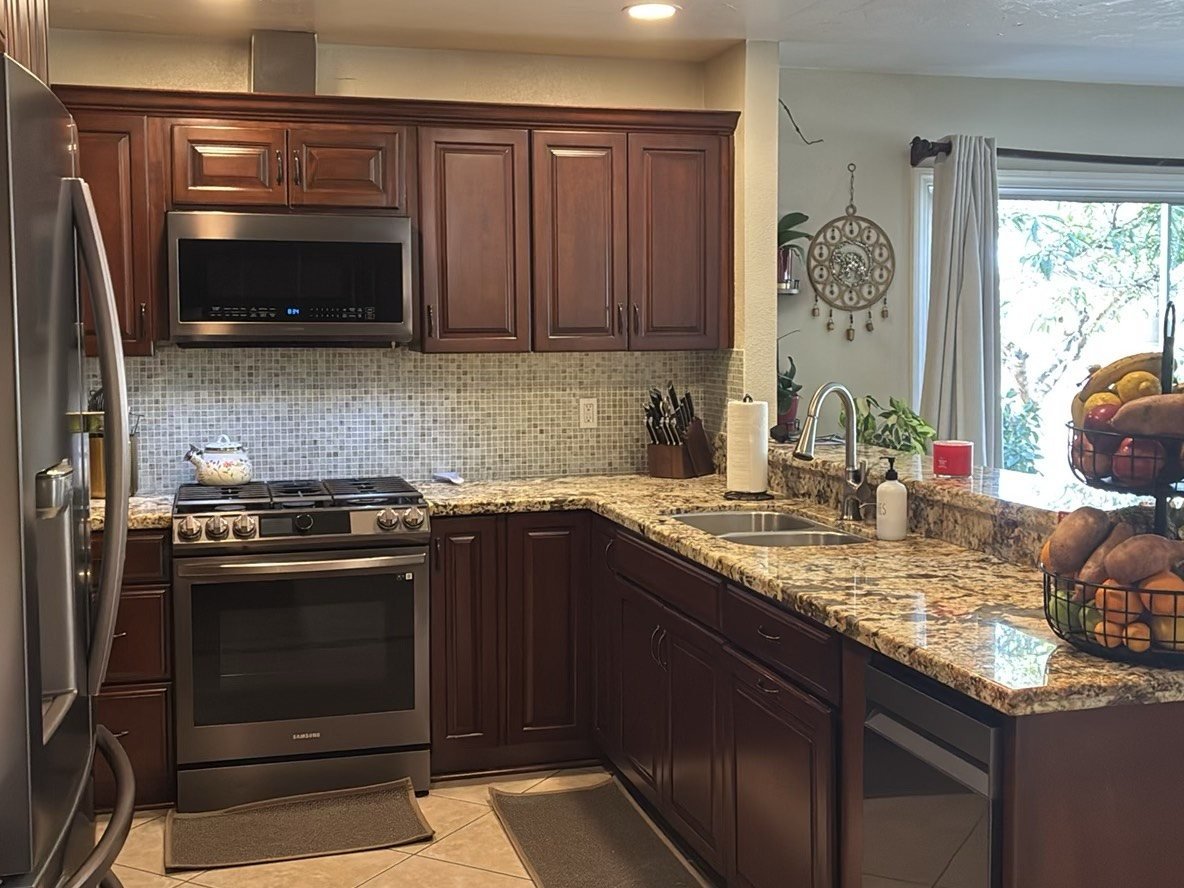 Bright updated kitchen with dark cherry wood cabinets, granite countertops, stainless steel appliances, and a large window